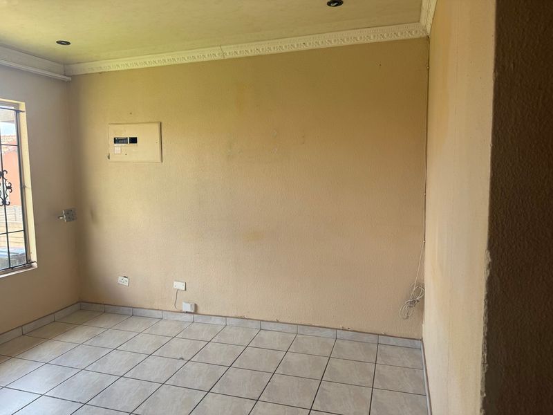 An empty living area featuring ceramic floor tiles, recessed lighting, and decorative coving, requiring cosmetic updates to the wall finishes.