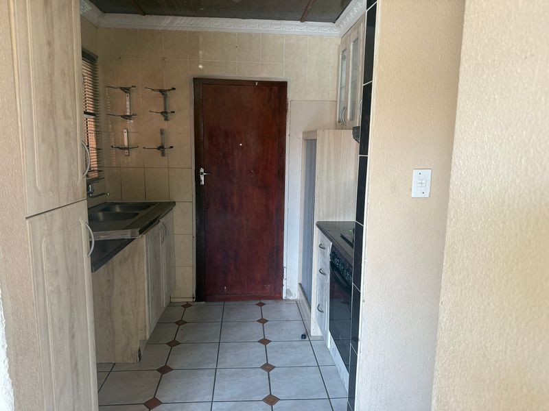 A compact kitchen featuring built-in cabinetry, a double sink, and a built-in oven, with tiled flooring and backsplash throughout.