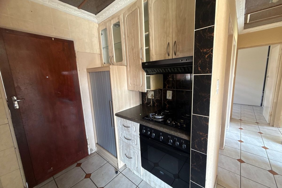 Compact kitchen featuring built-in cabinetry, a gas hob with extractor fan, and tiled flooring. The space is ready for a modern update.