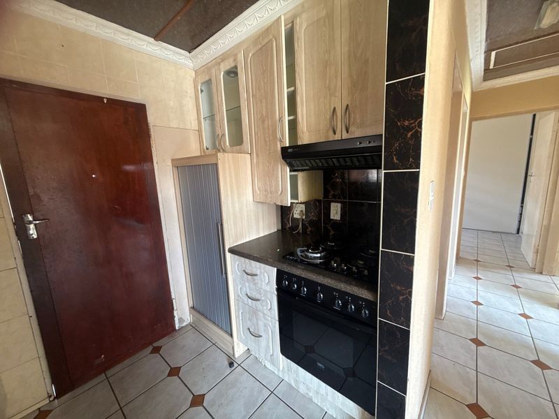 Compact kitchen featuring built-in cabinetry, a gas hob with extractor fan, and tiled flooring. The space is ready for a modern update.