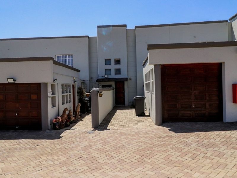 Front elevation of a townhouse featuring a paved driveway, two wooden garage doors, and a central pedestrian entrance.