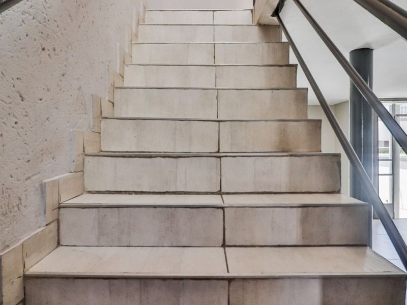 A staircase featuring tiled steps, a metal handrail, and a textured wall finish, leading towards an open entrance area.