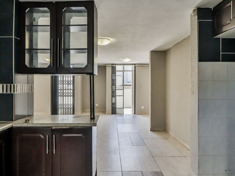 Open plan living and kitchen area featuring dark wood cabinetry, tiled flooring, and direct access to an outdoor space through a security gate.