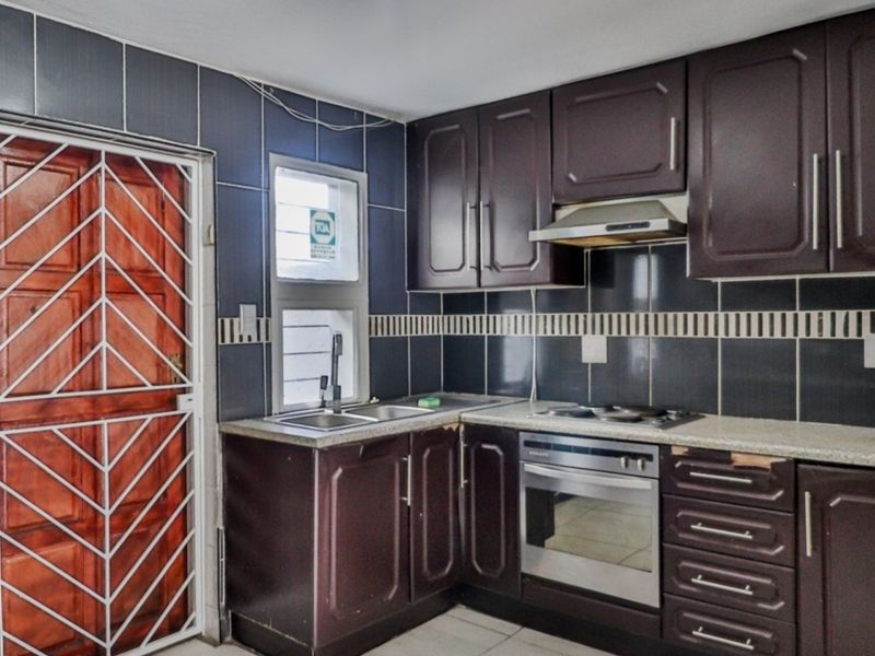 Functional kitchen featuring dark cabinetry, built-in oven, hob, extractor fan, and tiled backsplash, with direct access to an exterior security gate.