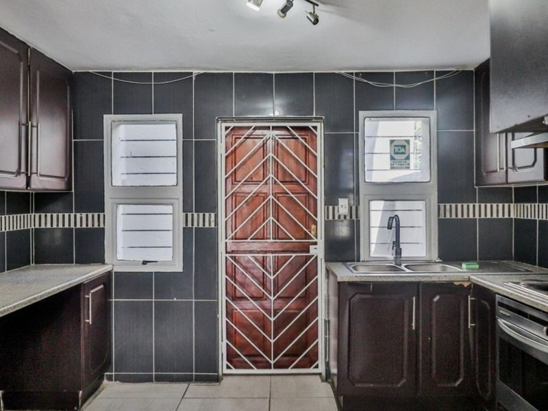 Functional kitchen featuring dark wood cabinetry, stone-look countertops, double sink, built-in oven, and tiled splashback with direct access to an exterior security gate.