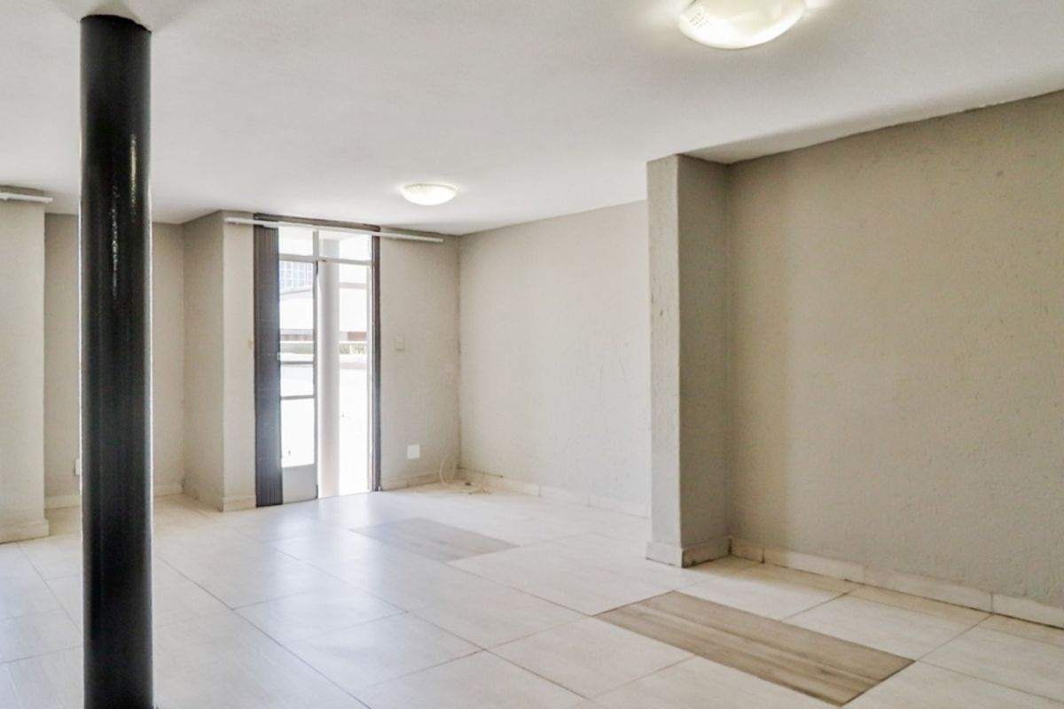 An empty, open-plan living area featuring neutral tiled flooring, a structural support column, and access to an outdoor space via a sliding glass door.