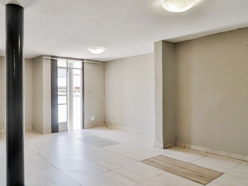 An empty, open-plan living area featuring neutral tiled flooring, a structural support column, and access to an outdoor space via a sliding glass door.