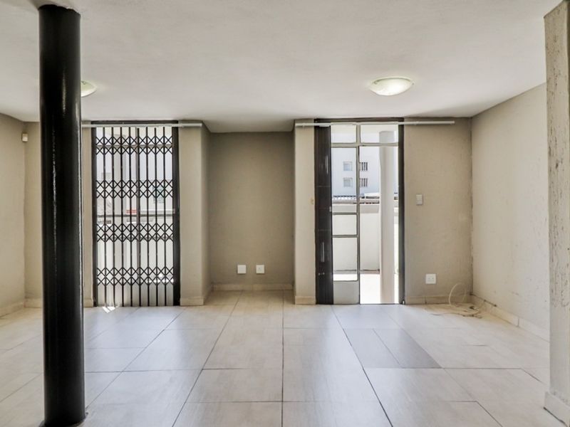 An empty, open-plan living area featuring neutral tiled flooring, a structural support column, and access to an outdoor space via a security gate.