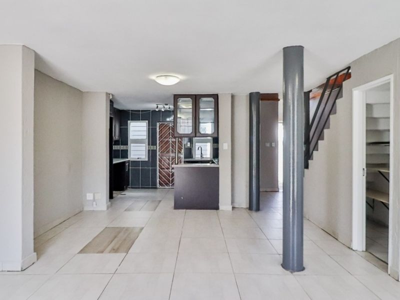 Spacious open-plan living area featuring tiled flooring, structural columns, a staircase, and a functional kitchen space with built-in cabinetry.
