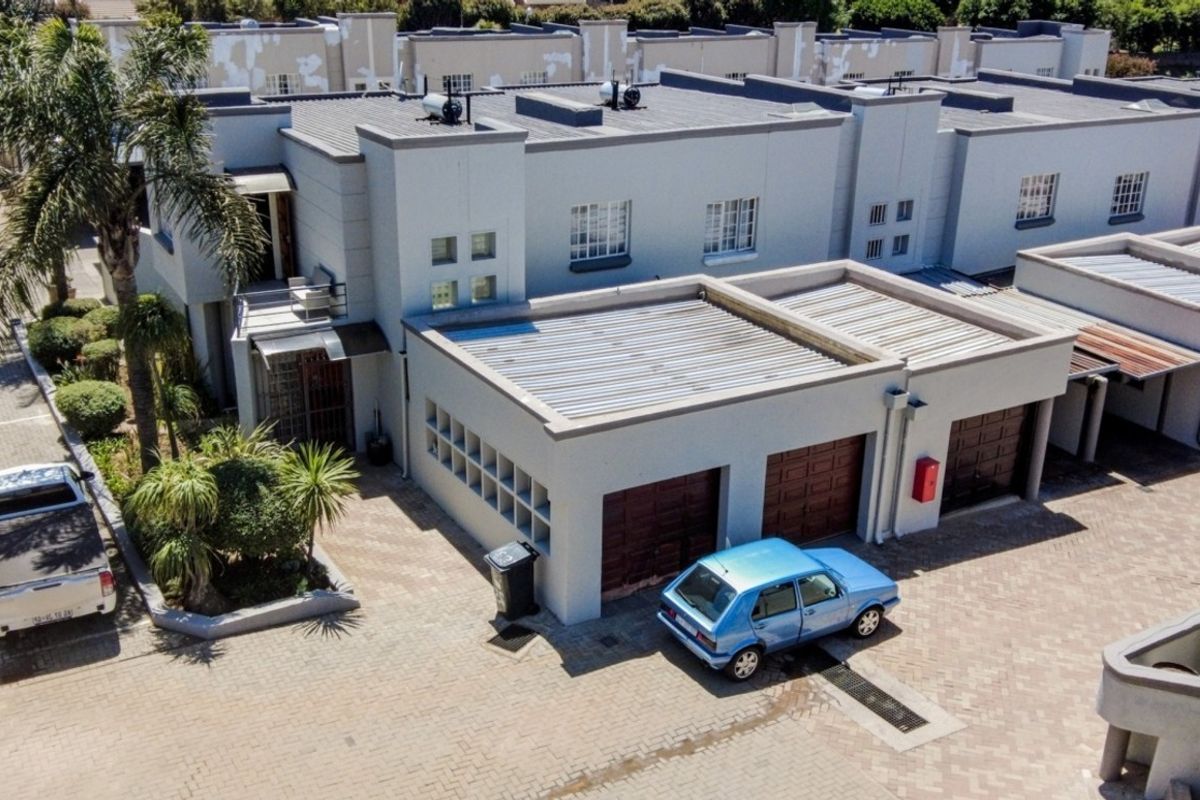Aerial view of a townhouse complex featuring paved driveways, double garages, and corrugated roofing with visible exterior paint maintenance required.