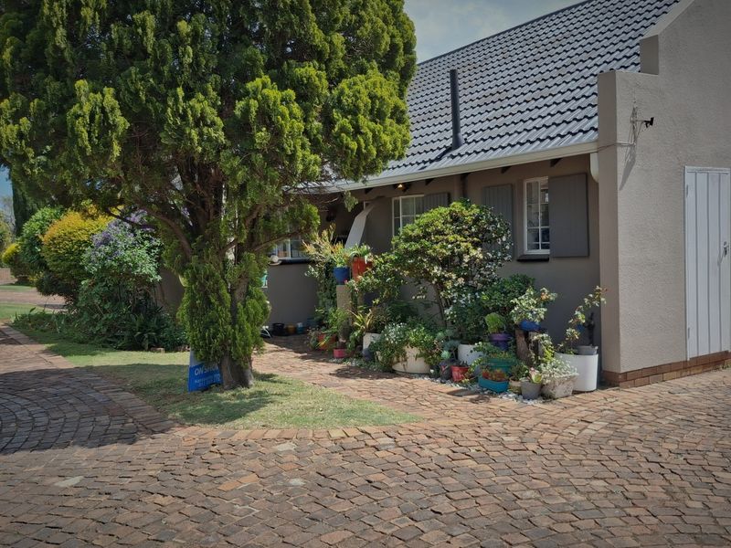 Front elevation of a small holding property featuring a cobblestone driveway, plastered walls, and a tiled roof with established garden landscaping.