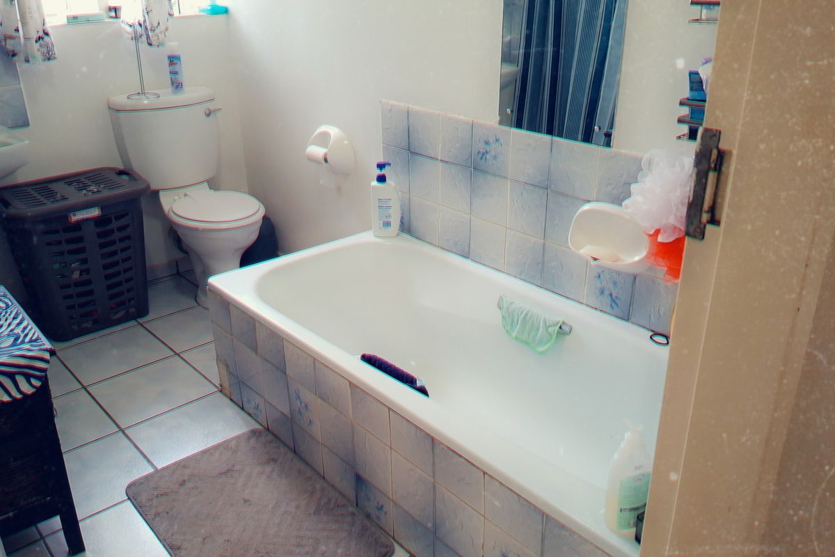 A functional bathroom featuring a pedestal basin, toilet, and a tiled built-in bathtub with dated finishes, requiring cosmetic updates.