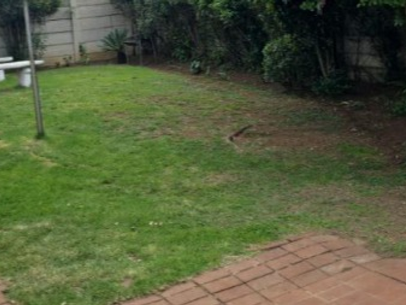A view of a residential garden featuring a lawn area, brick paving, and perimeter precast concrete walling.