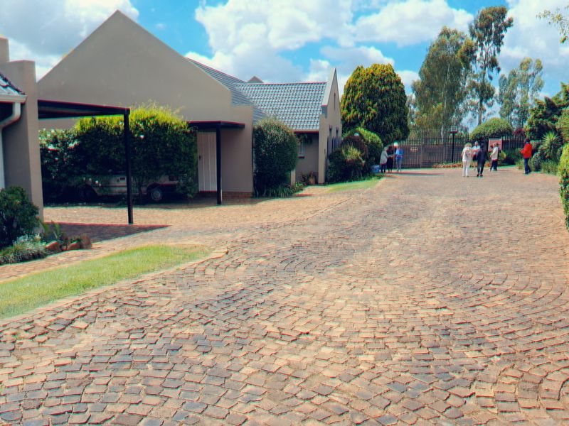A well-maintained exterior view of the property featuring a spacious cobblestone driveway, covered carport, and neatly landscaped garden areas.
