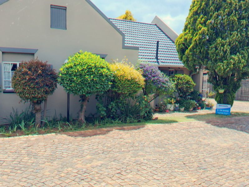 Front elevation of a well-maintained small holding property featuring a cobblestone driveway, tiled roof, and established garden landscaping.