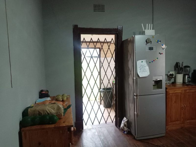 A kitchen area featuring wooden cabinetry and a security gate leading to an exterior space, showing signs of wear and dated finishes.