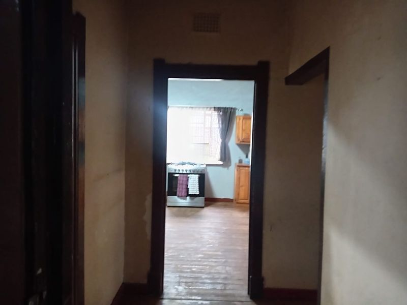 A view from a hallway looking into a kitchen area, featuring wooden door frames and original timber flooring in need of refurbishment.