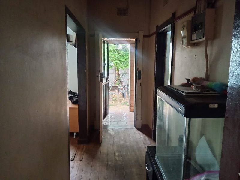 A narrow hallway featuring timber flooring and an exposed electrical distribution board, leading directly to an exterior doorway.
