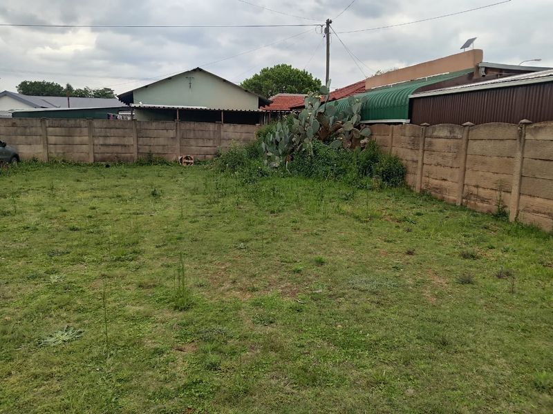 A rear garden area featuring a precast concrete boundary wall and an unmaintained lawn with overgrown vegetation.