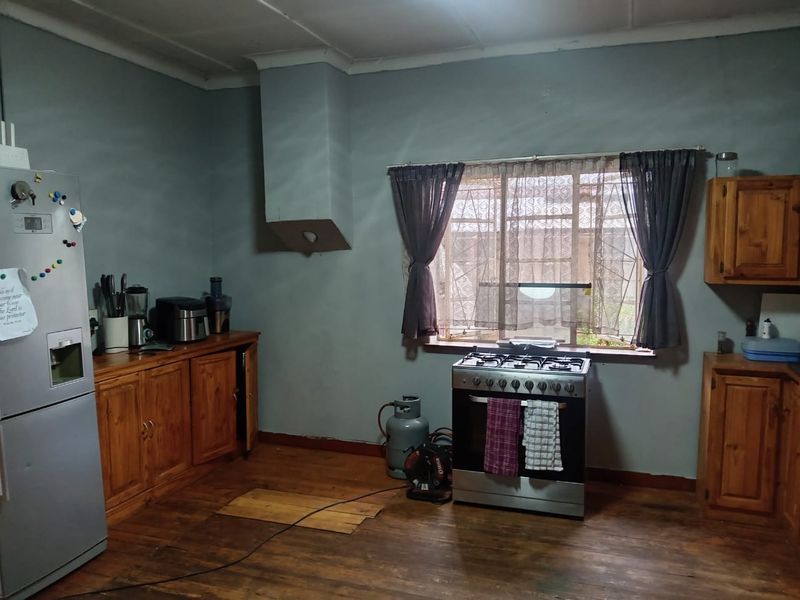 A kitchen featuring wooden cabinetry, a gas stove, and timber flooring, currently requiring cosmetic updates and repairs to the flooring and wall finishes.