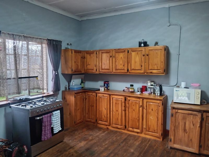 A functional kitchen featuring wooden cabinetry, a gas stove, and timber flooring, offering potential for modernization and aesthetic improvement.