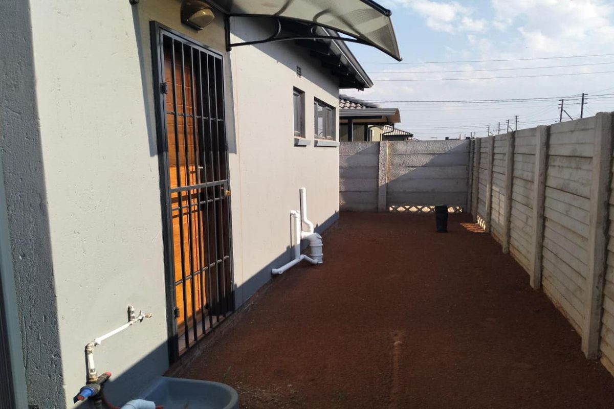 A side exterior view of the property featuring a security gate, external plumbing, and a precast concrete boundary wall.