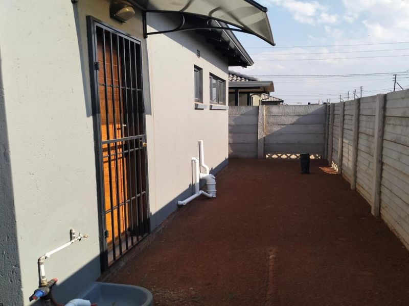 A side exterior view of the property featuring a security gate, external plumbing, and a precast concrete boundary wall.