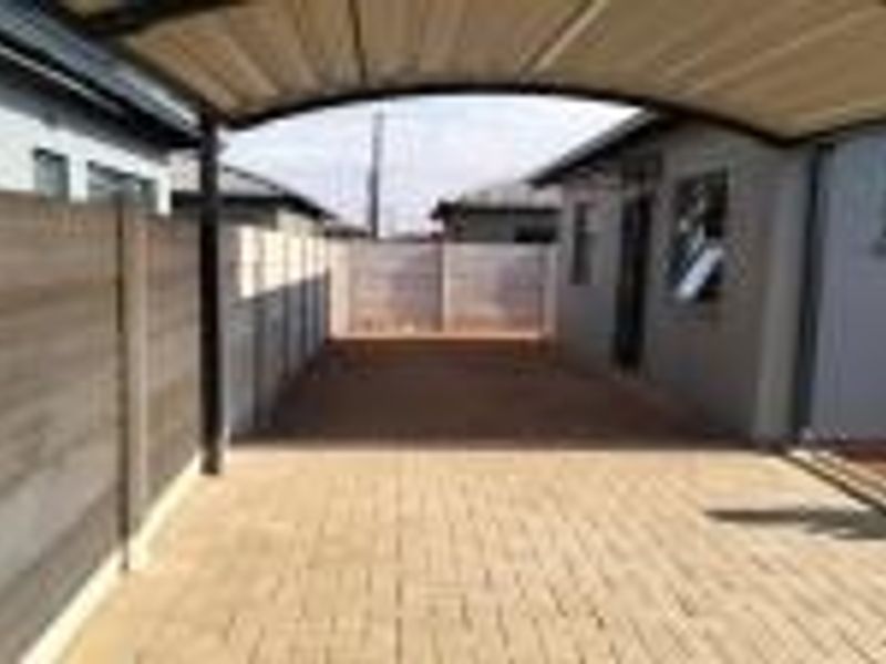 A paved driveway area featuring a covered carport and secure precast concrete boundary walls.