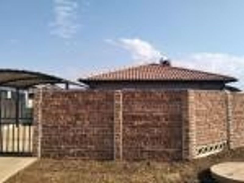Front exterior view of the property featuring a brick boundary wall, metal carport, and concrete driveway leading to the main entrance.