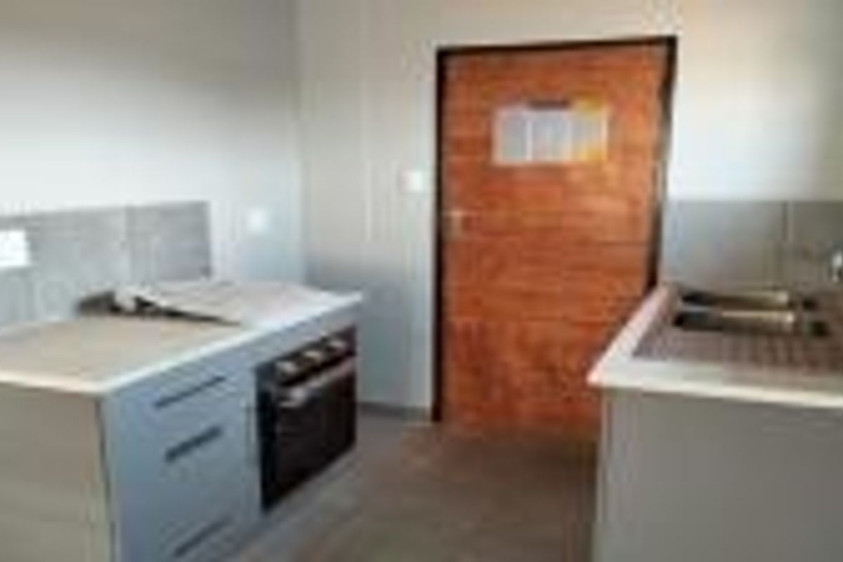 A functional kitchen area featuring built-in cabinetry, a hob, an oven, and a double sink with tiled splashbacks.