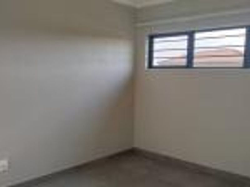 A vacant bedroom featuring neutral wall paint, a horizontal window with security burglar bars, and a standard electrical outlet.