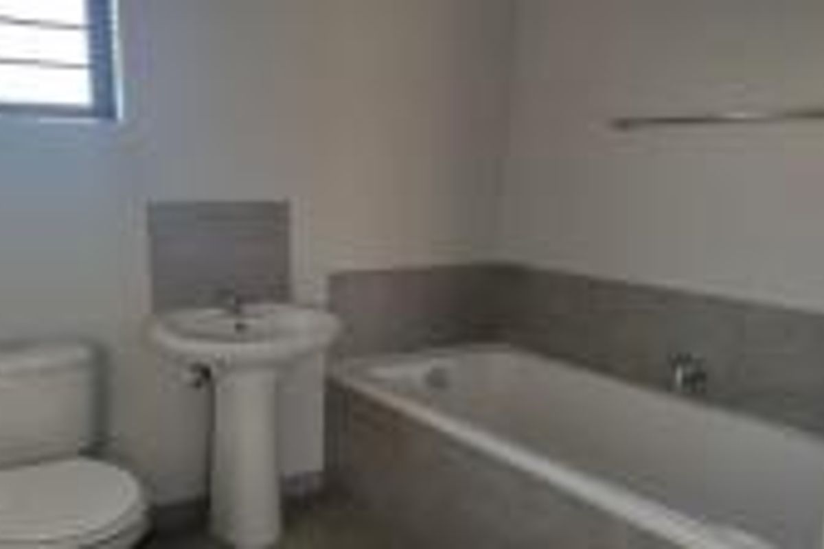 A clean, functional bathroom featuring a pedestal basin, bathtub, and toilet with neutral wall tiling.