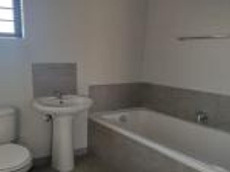 A clean, functional bathroom featuring a pedestal basin, bathtub, and toilet with neutral wall tiling.