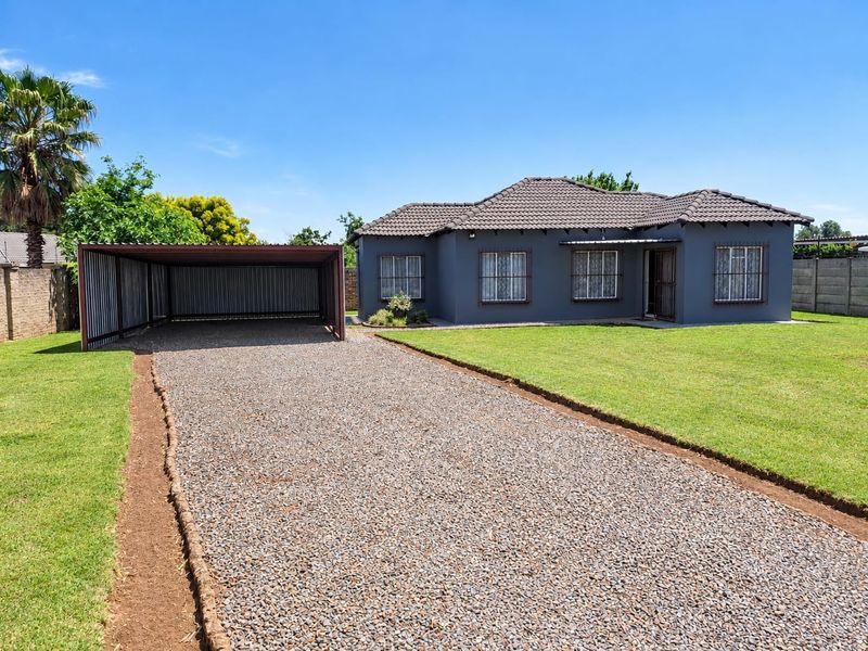 Front view of a well-maintained house featuring a gravel driveway, a spacious carport, and a neat lawn with secure window bars.