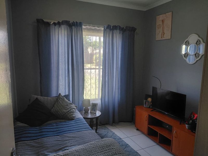 A functional bedroom featuring tiled flooring and a window fitted with security bars, providing natural light and essential security.