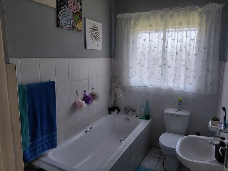 A functional bathroom featuring a built-in bathtub, pedestal basin, and toilet with neutral wall tiling and tiled flooring.