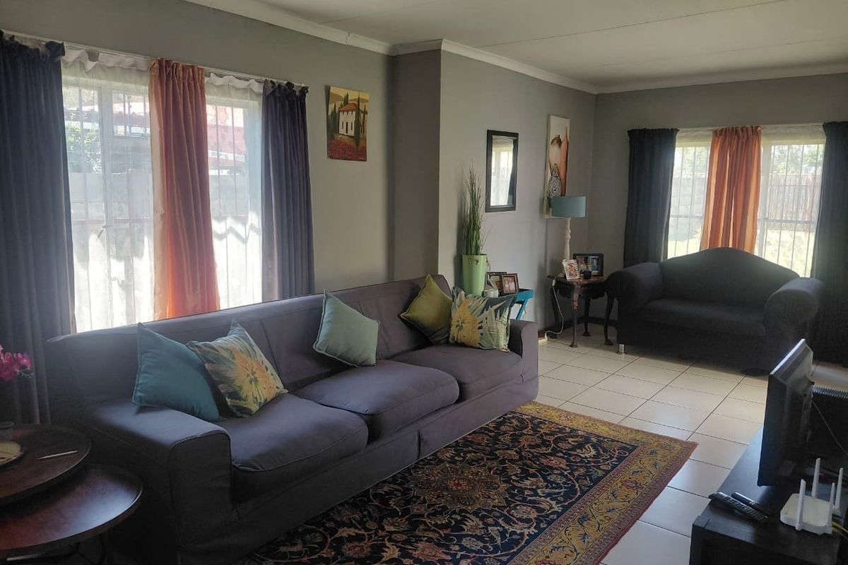 A spacious living room featuring tiled flooring, neutral wall tones, and large windows fitted with security bars, providing ample natural light.