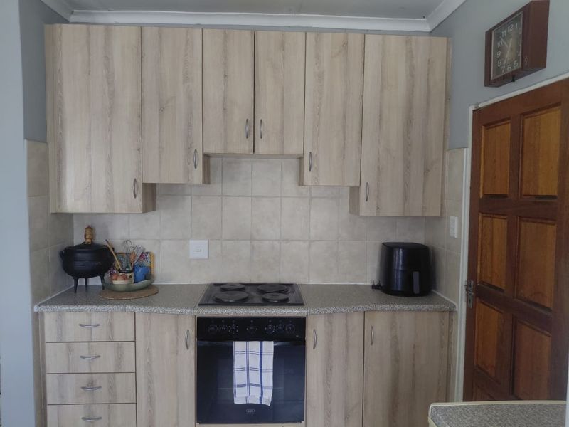 A functional kitchen featuring light wood-grain cabinetry, a built-in oven with electric hob, and neutral tiled splashbacks.