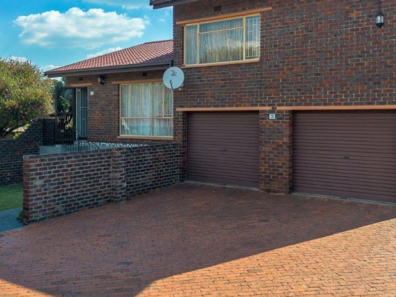 Front exterior view of a brick townhouse featuring a double garage with roller shutter doors and a paved driveway.