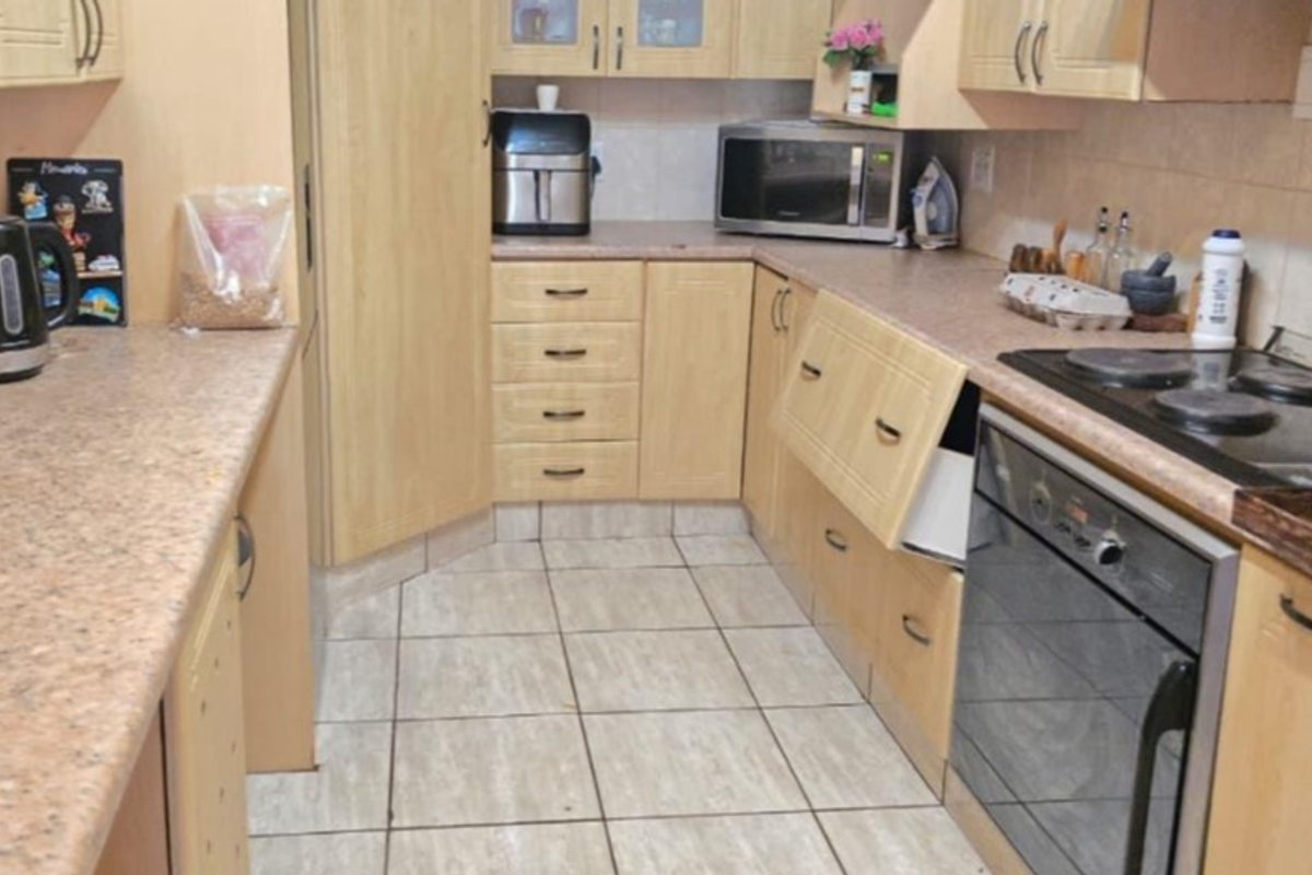 A functional kitchen featuring laminate cabinetry, tiled flooring, and built-in cooking appliances, currently requiring minor repairs to cabinet hardware.