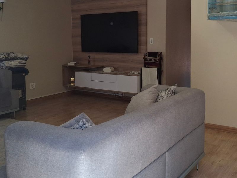 A comfortable living room featuring laminate flooring and a modern built-in media unit with a wall-mounted television.