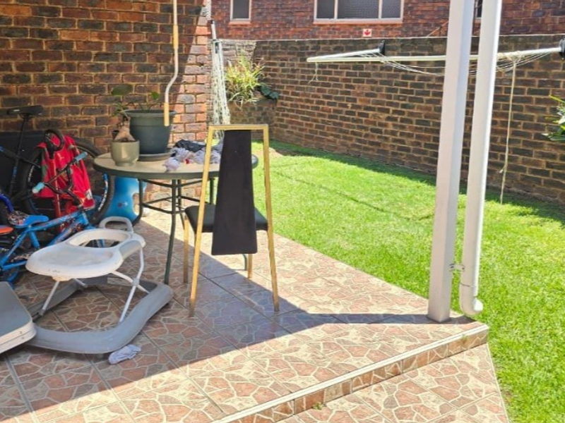 A covered patio area featuring tiled flooring and a brick boundary wall, providing direct access to the rear garden space.