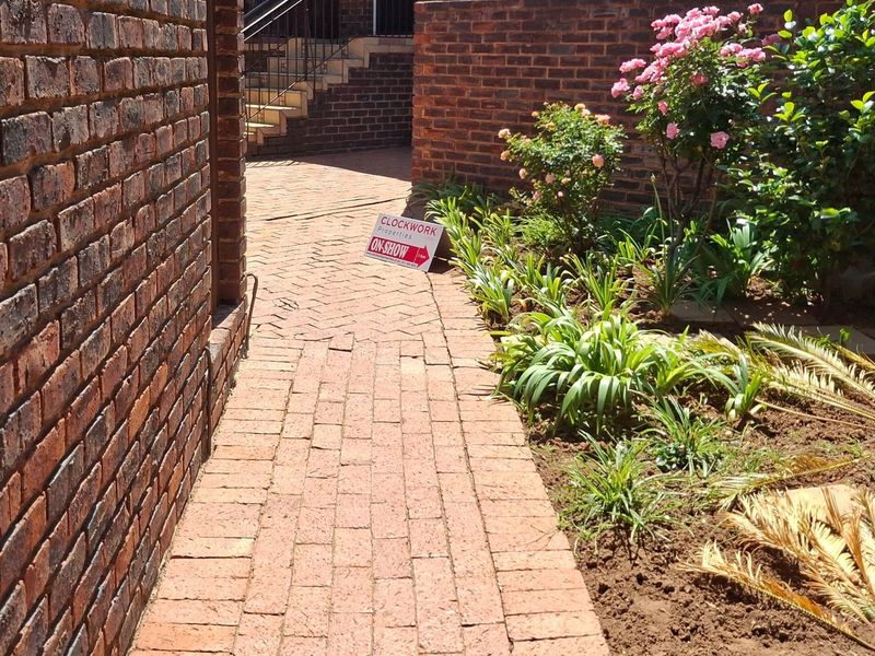 A brick-paved walkway leading to a staircase, framed by face brick walls and established garden beds.
