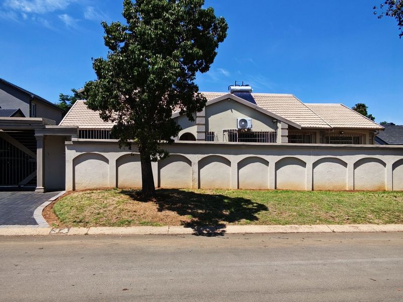 Front elevation of a residential property featuring a paved driveway, carport, and a decorative perimeter wall with a tiled roof house behind.
