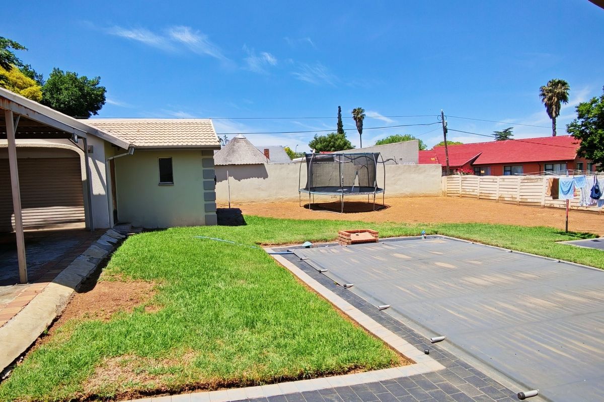Rear garden area featuring a swimming pool with cover, a carport, and a boundary wall, providing a functional outdoor space.