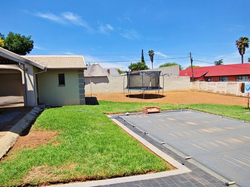 Rear garden area featuring a swimming pool with cover, a carport, and a boundary wall, providing a functional outdoor space.