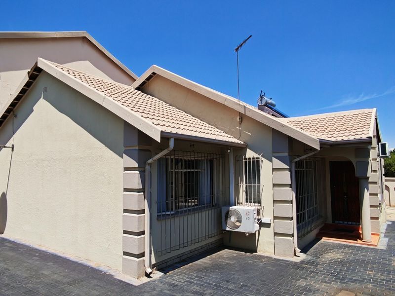 Front elevation of a residential house featuring a tiled roof, paved driveway, and installed security bars on windows.