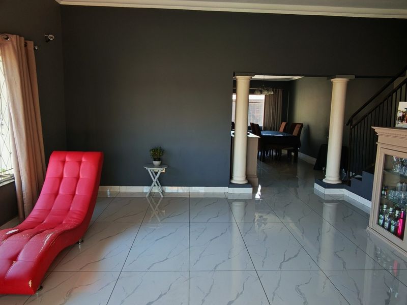 Spacious open-plan living area featuring modern marble-look floor tiles, decorative columns, and a staircase, creating a seamless flow between living and dining spaces.