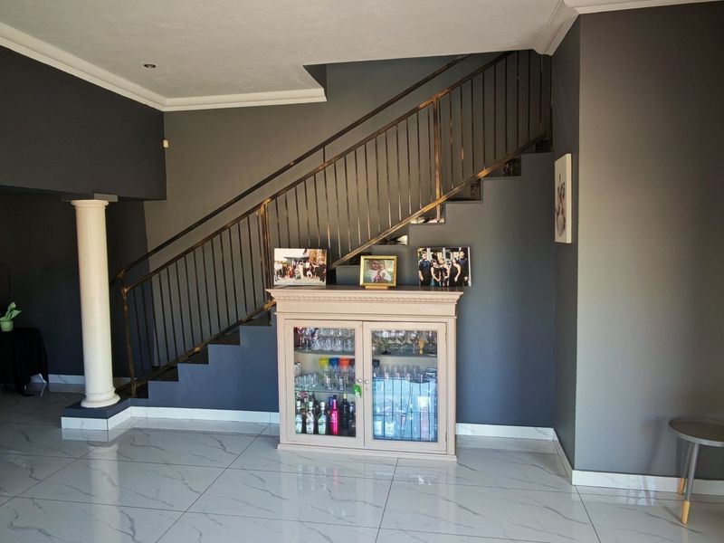 Spacious living area featuring a modern staircase with metal balustrade, decorative columns, and polished porcelain floor tiles.
