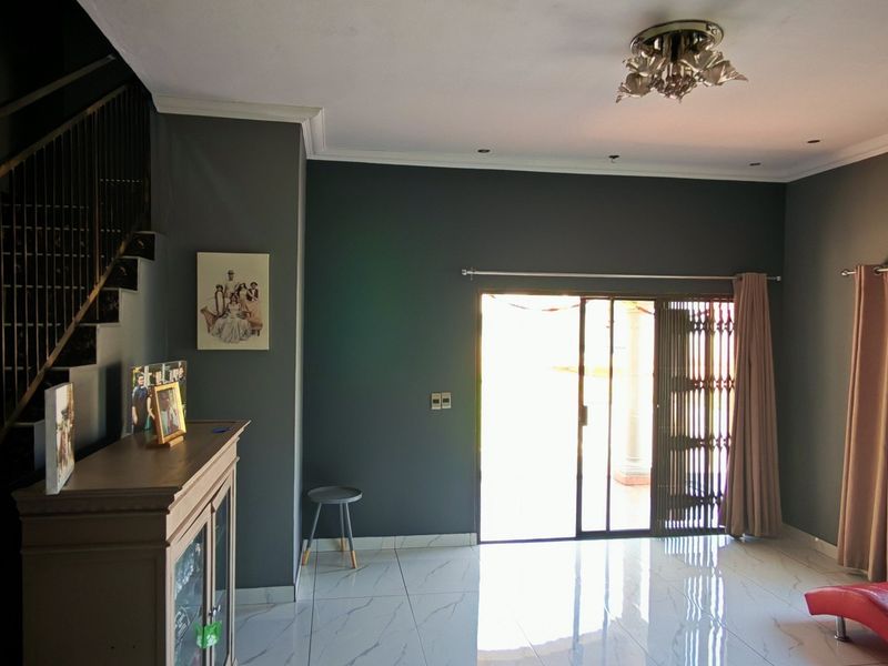 Spacious living room featuring modern tiled flooring, a sleek staircase with metal balustrade, and direct access to the outdoor area via sliding glass doors.